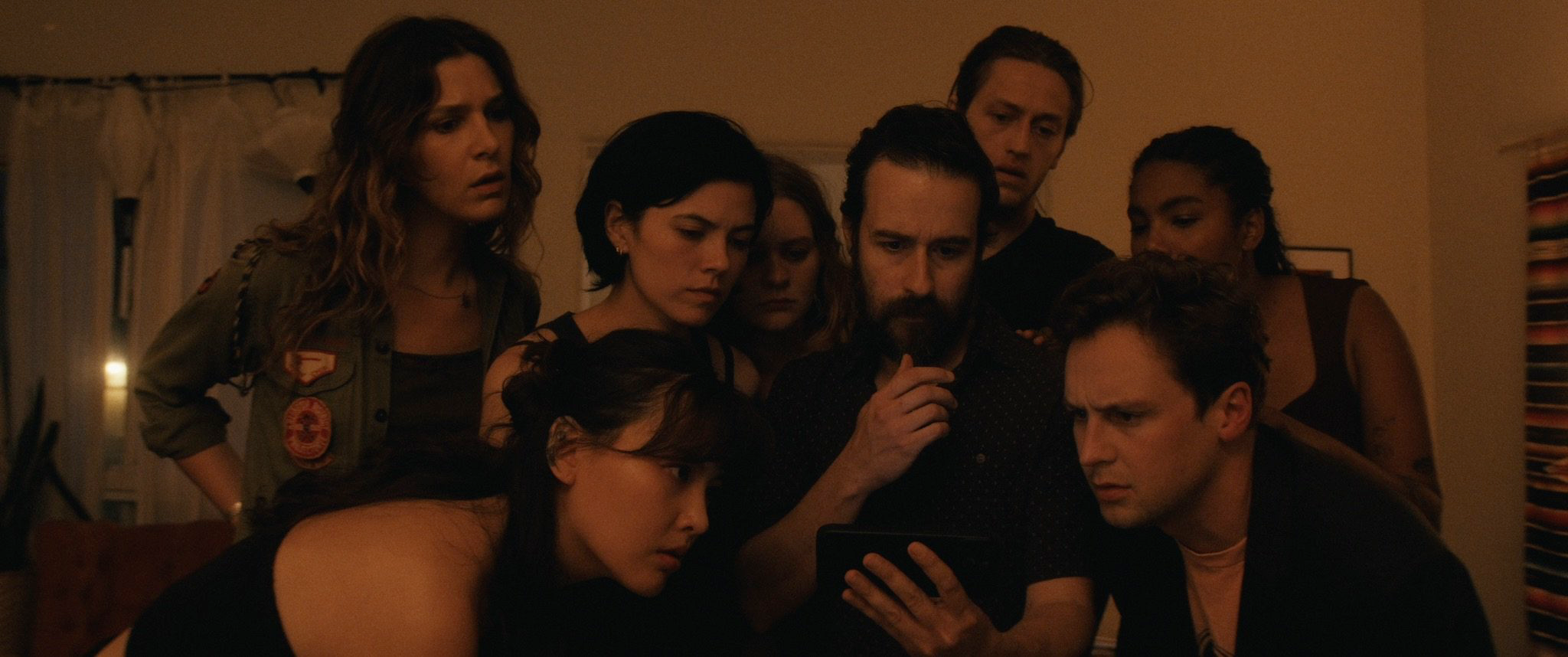 Still from "The Plan" depicting a group of young adults gathered around a phone.